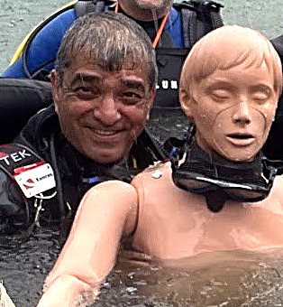 Kami in scuba gear beside a rescue training manikin at a quarry dive site.
